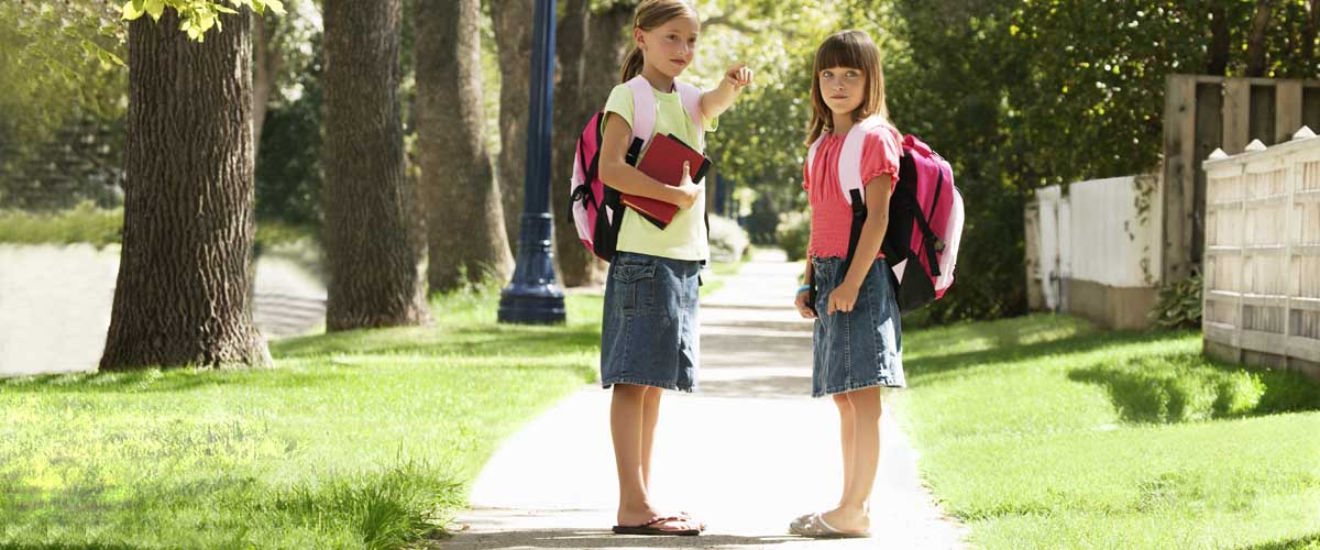 two 8 year old girls, walking home from school, on the sidewalk, pointing with a wave