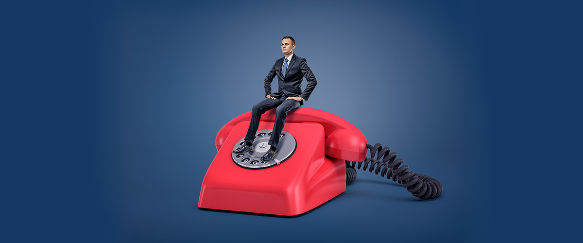 miniature executive sitting on top of a classic red telephone, having patience