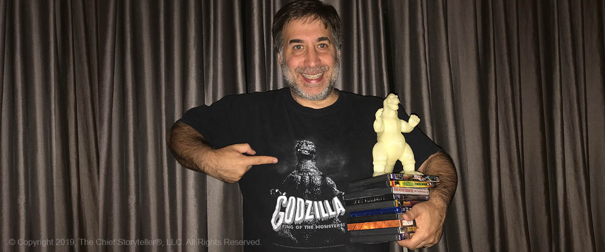 ira koretsky holding several godzilla dvds, a glow in the dark godzilla, and pointing to Godzilla on his t-shirt