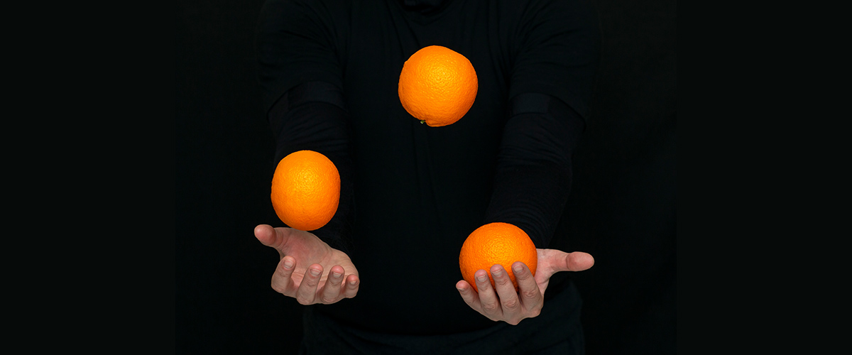black background, near silhoutte of a man juggling three oranges, representing the challenges of project management, from our MCA Chicago Leaders to the Power of Story workshop webinar